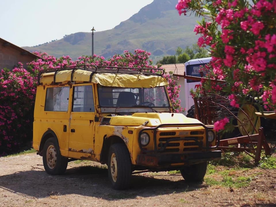 A yellow vintage car parked among blooming oleander at a farm stay in Sicily