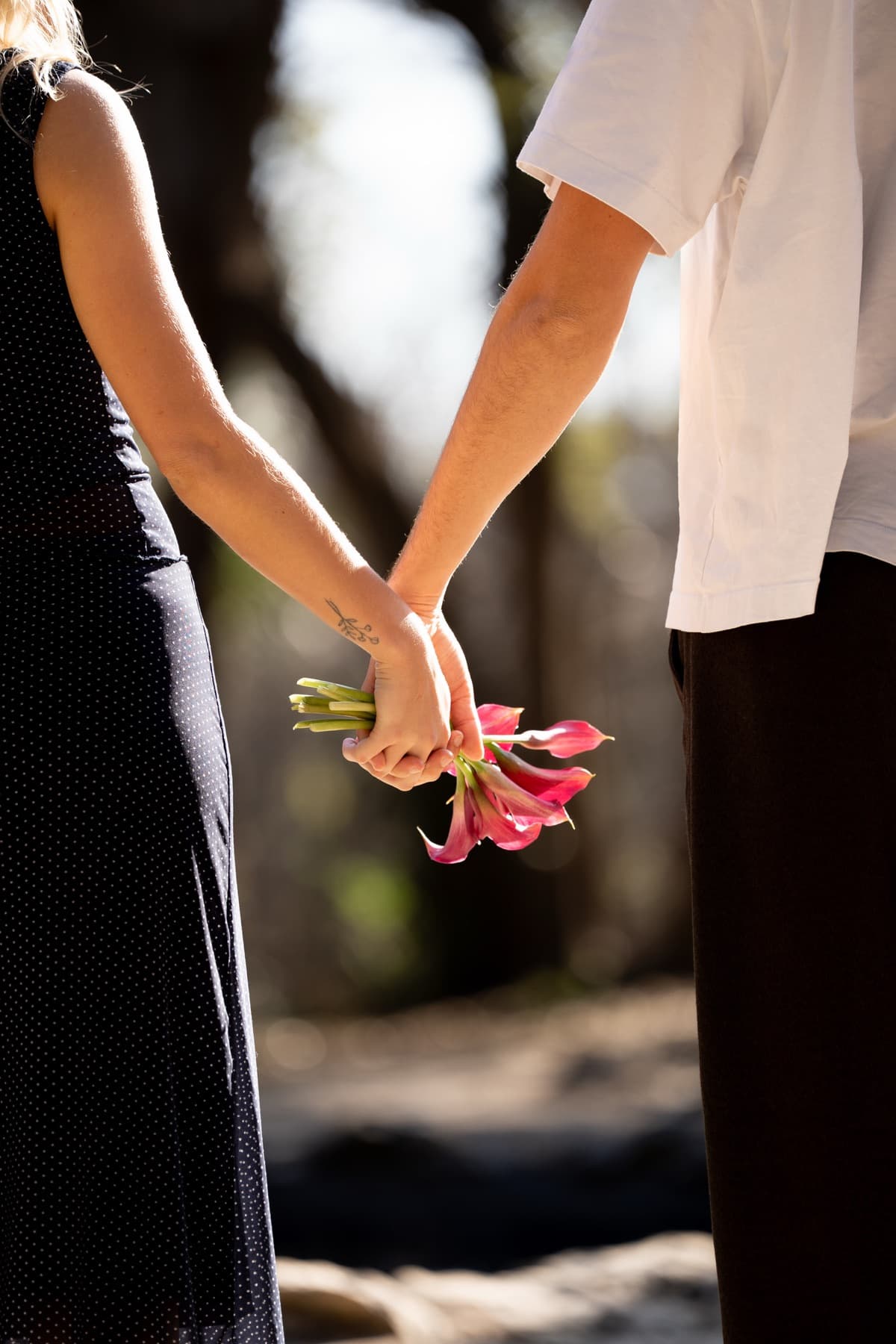 A close-up of a couple holding hands behind their backs with a bouquet of flowers