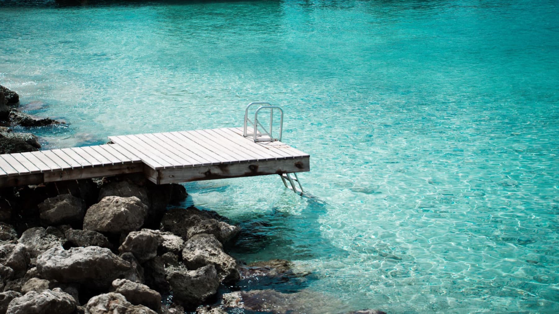 A wooden dock with a ladder over clear turquoise water at Divi Dive Resort in Bonaire