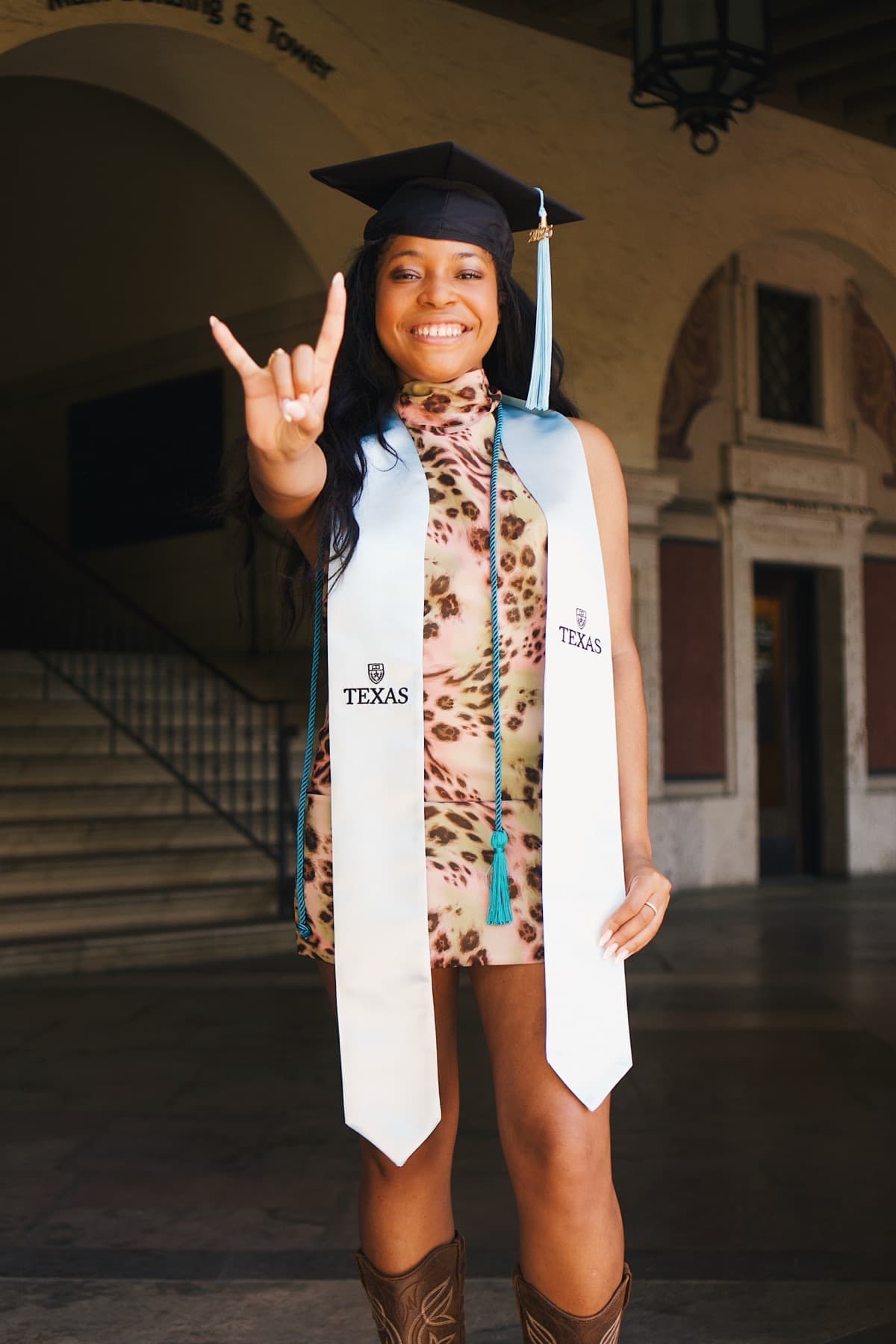 A senior portrait in cap and gown throwing a hook 'em horns hand sign
